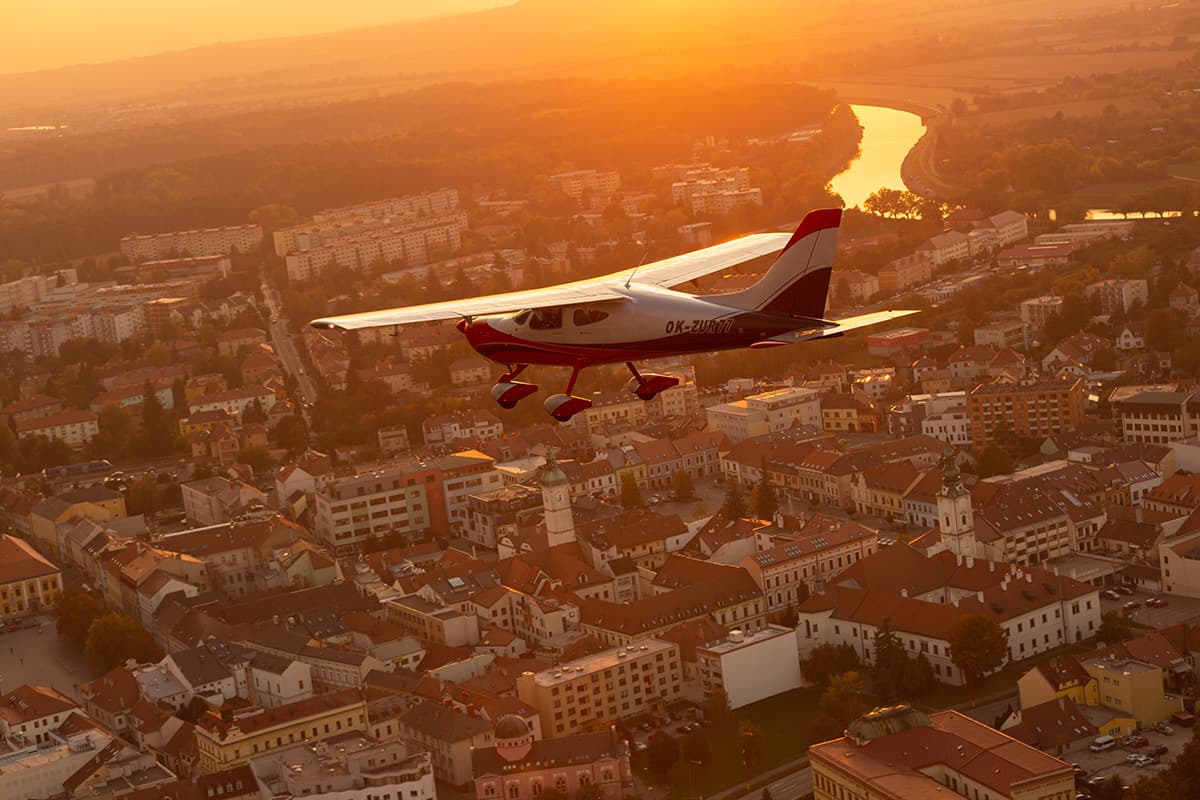Bristell B8M above a town and river at sunset