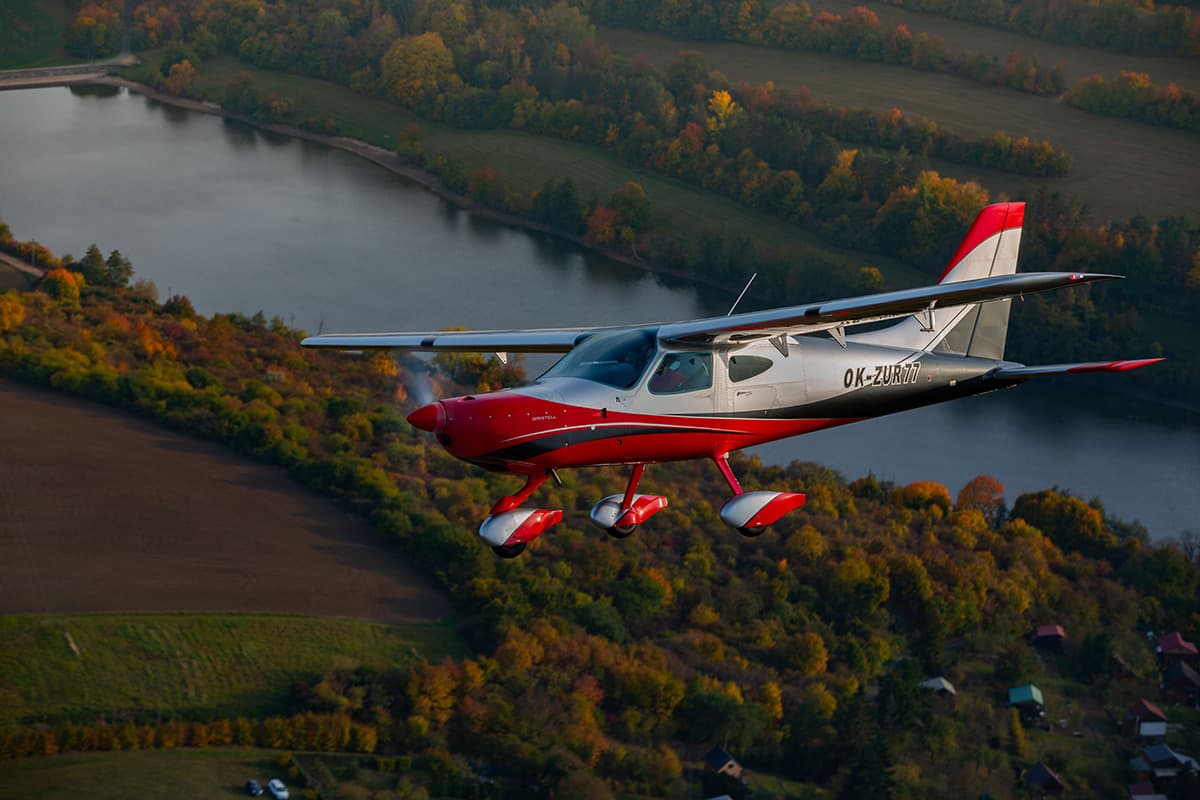Bristell B8M in flight over a lake and fields